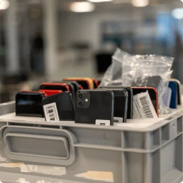 Eine Box mit gebrauchten Smartphones. Sie wurden in dafür vorgesehenen Fächern stehend aneinandergereiht. Zu sehen ist entweder die Vorder- oder die Rückseite.